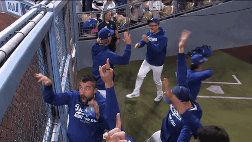 A Group Of People Wearing Dodgers Hoodies Are Dancing On A Baseball Field GIF