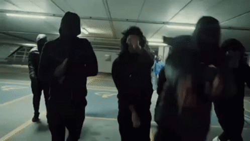 A Group Of People Wearing Hoodies Are Walking In A Parking Garage . GIF