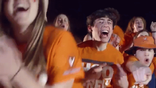 a group of people wearing orange shirts and hats are standing in a crowd .