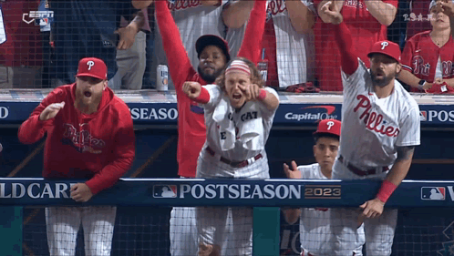A Group Of Phillies Baseball Players Are Standing In The Dugout With Their Arms In The Air GIF