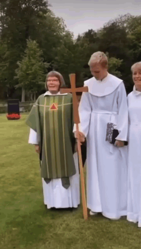 A Group Of Priests Are Standing In A Grassy Field Holding A Cross GIF