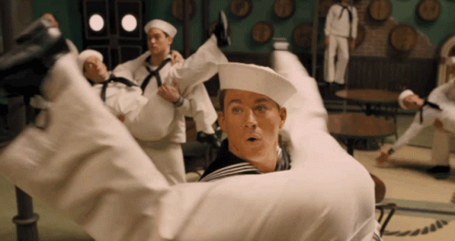 A Group Of Sailors Are Holding A Man In Their Arms In A Room With Barrels On The Wall GIF