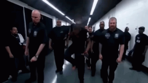 A Group Of Security Guards Are Walking Down A Hallway In A Building . GIF