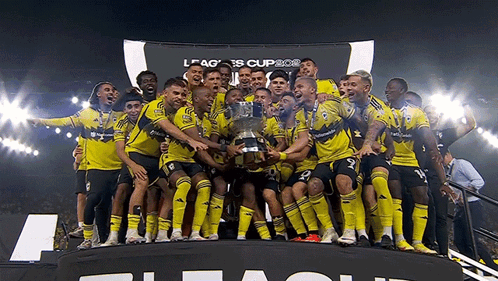 A Group Of Soccer Players Are Holding A Trophy In Front Of A Banner That Says League Cup GIF