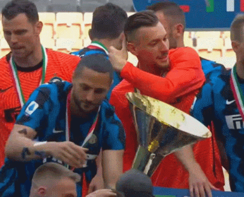A Group Of Soccer Players Are Hugging Each Other While Holding A Trophy . GIF