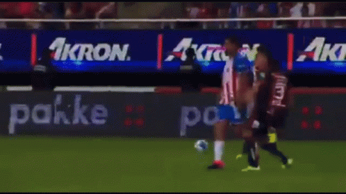 A Group Of Soccer Players Are Playing On A Field With An Ad For Akron Behind Them GIF