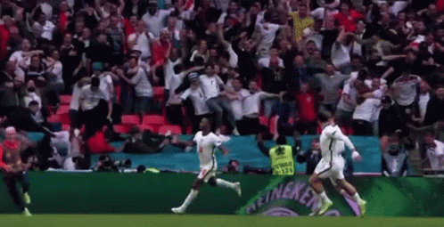 A Group Of Soccer Players Are Running On A Field In Front Of A Crowd Of People . GIF