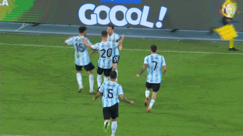 A Group Of Soccer Players Celebrate A Goal In Front Of A Jogo Oficial Sign GIF