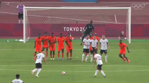 a group of soccer players on a field with tokyo 2020 written on the wall behind them
