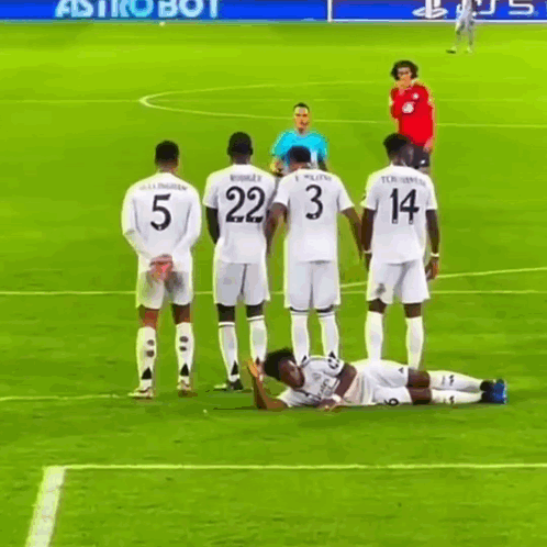 a group of soccer players standing around a player laying on the field