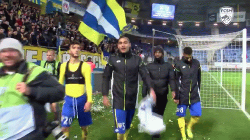 A Group Of Soccer Players Walking On A Field With A Fcsm Logo GIF