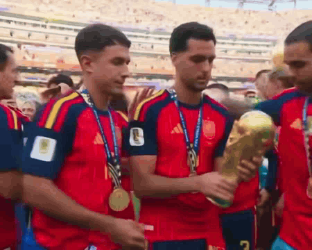 A Group Of Soccer Players With Medals Around Their Necks Are Holding A Trophy With The Number 7 On It GIF