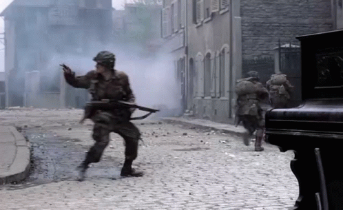 A Group Of Soldiers Are Running Down A Cobblestone Street With Smoke Coming Out Of The Buildings GIF