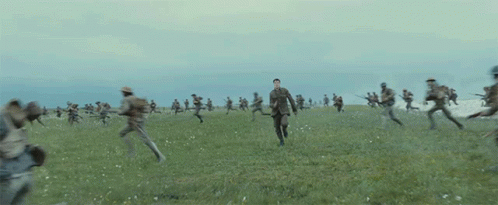 A Group Of Soldiers Are Running In A Field While An Explosion Takes Place . GIF