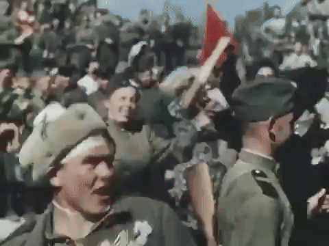 A Group Of Soldiers Are Standing In A Crowd Holding Up Flags GIF