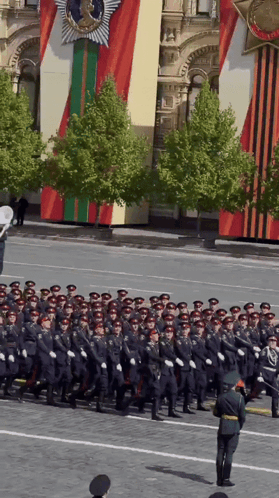 A Group Of Soldiers March Down A Street In Front Of A Building GIF