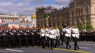 A Group Of Soldiers Marching Down A Street In Front Of A Building With The Word Russia On It GIF