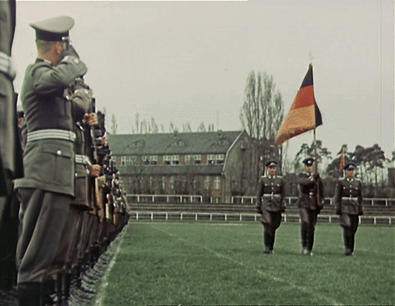 A Group Of Soldiers Marching In A Field With A Flag In The Background GIF