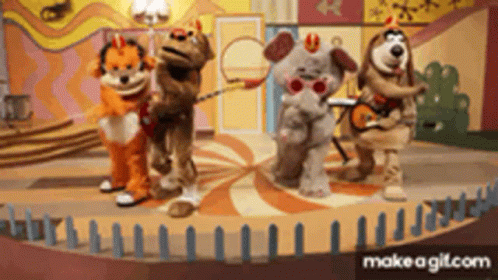 a group of stuffed animals are standing on a stage with dominoes in the background