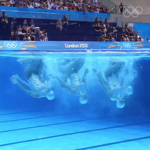 A Group Of Synchronized Swimmers Are Performing In A Pool With A Sign That Says London 2012 GIF