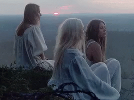 A Group Of Three Women Are Sitting On Top Of A Hill Looking At The Sunset . GIF