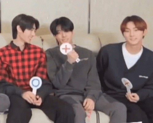 A Group Of Three Young Men Are Sitting On A Couch Holding Signs . GIF