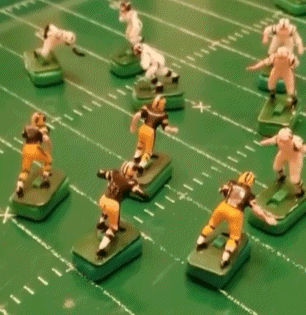 a group of toy football players on a green field with one wearing a black jersey with the number 9 on it