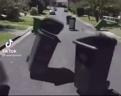 A Group Of Trash Cans Are Sitting On The Side Of A Road . GIF