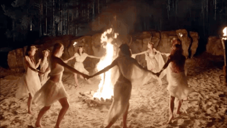 A Group Of Women Are Dancing Around A Fire On The Beach GIF