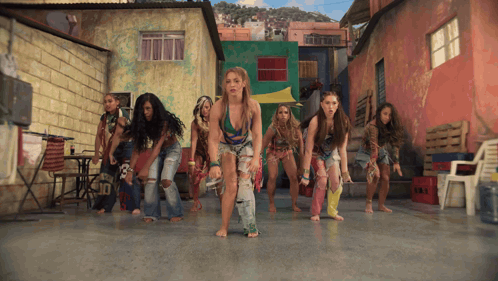 a group of women are dancing barefoot in front of a building that says ' tnt ' on it