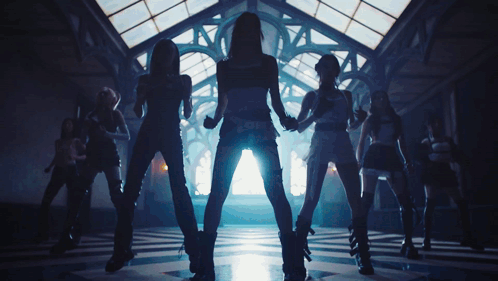 A Group Of Women Are Dancing In A Dark Room With A Light Shining Through The Windows GIF
