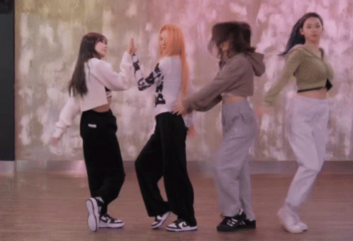 A Group Of Women Are Dancing In A Room With A Pink Wall Behind Them GIF