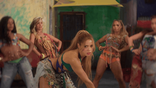a group of women are dancing in front of a green wall and a yellow umbrella