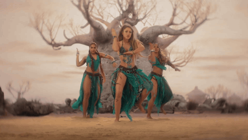 a group of women are dancing in front of a tree in the desert