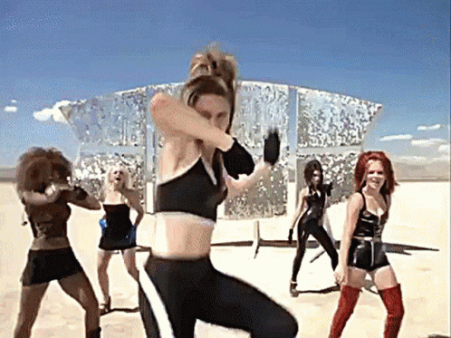 A Group Of Women Are Dancing In The Desert In Front Of A Mirrored Building . GIF