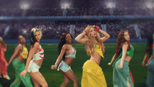 a group of women are dancing on a field and one of them is wearing a yellow skirt