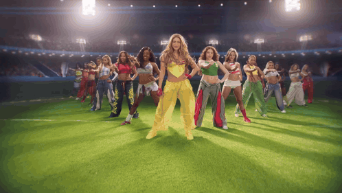 a group of women are dancing on a field with one wearing a yellow outfit