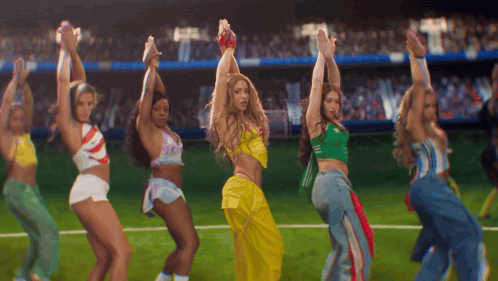a group of women are dancing on a field with their hands in the air