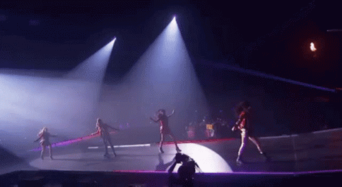 A Group Of Women Are Dancing On A Stage In A Dark Room With Purple Lights . GIF