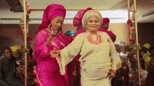A Group Of Women Are Dancing Together In A Room With Flowers . GIF