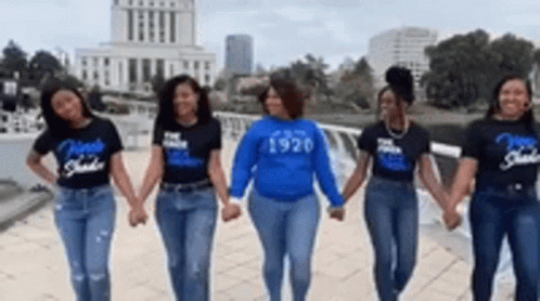 A Group Of Women Are Holding Hands In Front Of A Building . GIF