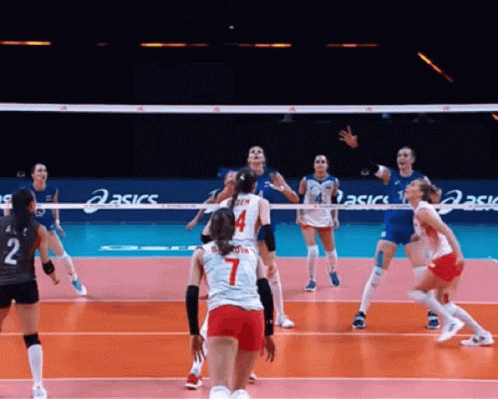 A Group Of Women Are Playing Volleyball On A Court With Asics Signs In The Background . GIF