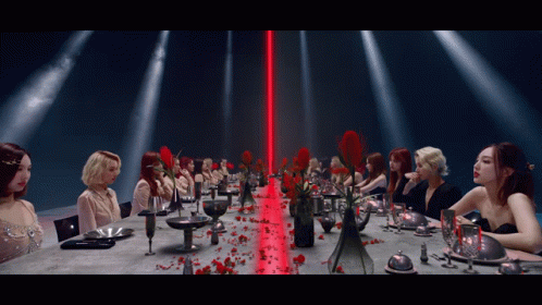 A Group Of Women Are Sitting At A Long Table With A Red Light Behind Them GIF