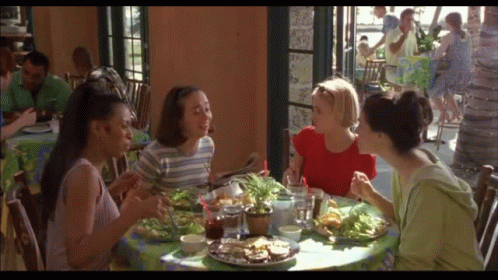 A Group Of Women Are Sitting At A Table With Plates Of Food GIF