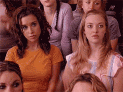 A Group Of Women Are Sitting In A Room And One Of Them Is Wearing An Orange Shirt GIF