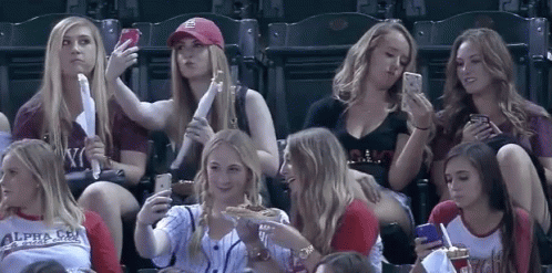 A Group Of Women Are Sitting In A Stadium And One Of Them Is Wearing A Shirt That Says Alpha Chi GIF