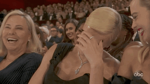 A Group Of Women Are Sitting In A Theatre Laughing And One Of Them Is Wearing A Ring On Her Finger GIF