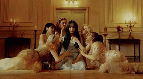 A Group Of Women Are Sitting On The Floor Looking At A Woman In A Blue Dress GIF