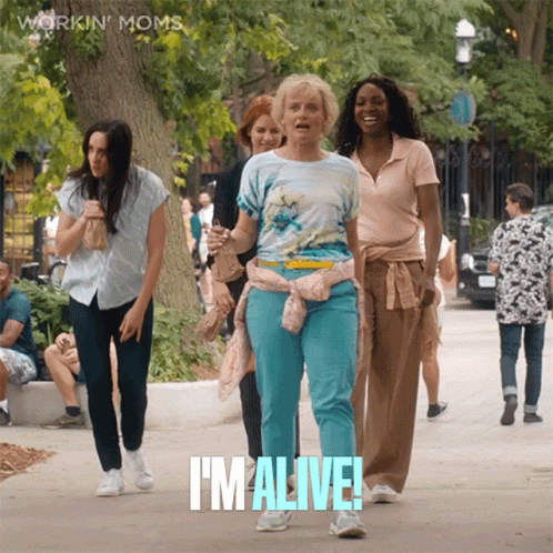 A Group Of Women Are Walking Down A Sidewalk And One Of Them Is Saying I 'M Alive GIF