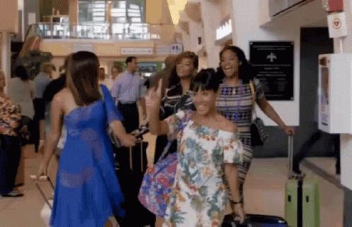 A Group Of Women Are Walking Through An Airport With Luggage And Smiling GIF